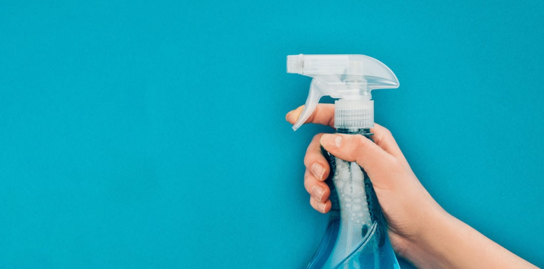 cropped image of woman holding spray bottle near washing sponges isolated on blue