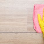 Hand in pink rubber protective glove wiping wooden floor with dry rag. Closeup. Empty place for text or logo. Top down view.