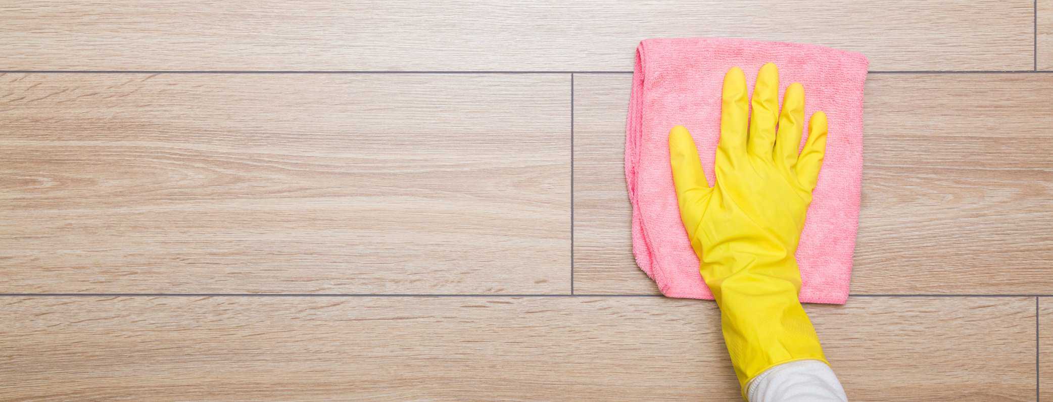 Hand in pink rubber protective glove wiping wooden floor with dry rag. Closeup. Empty place for text or logo. Top down view.