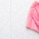 Woman hand in pink rubber protective glove wiping light gray ceramic tiles wall with dry rag. Closeup. Spring general or regular cleanup. Empty place for text or logo.